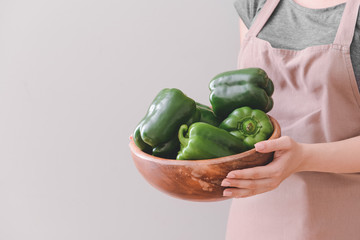 Woman with bowl of green bell pepper on light background