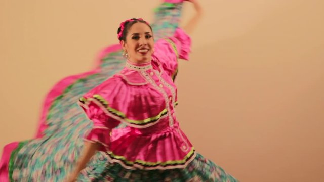 Joven mujer mexicana latina en traje regional folcl&oacute;rico en fondo rosa haciendo orlas con vestido baile danza t&iacute;pico