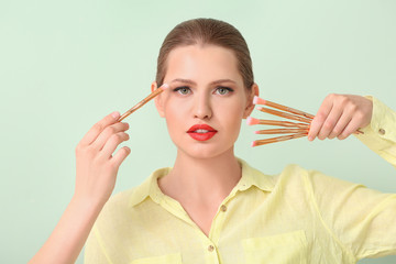 Obraz premium Beautiful young woman with makeup brushes on color background