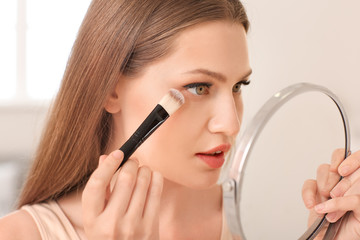 Beautiful young woman applying makeup at home