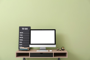 Modern computer and to-do list on table near color wall