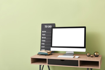 Modern computer and to-do list on table near color wall