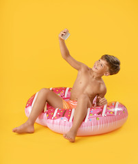Fototapeta na wymiar Cute little boy with inflatable ring taking selfie on color background