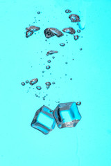 Falling of ice cubes into water on color background