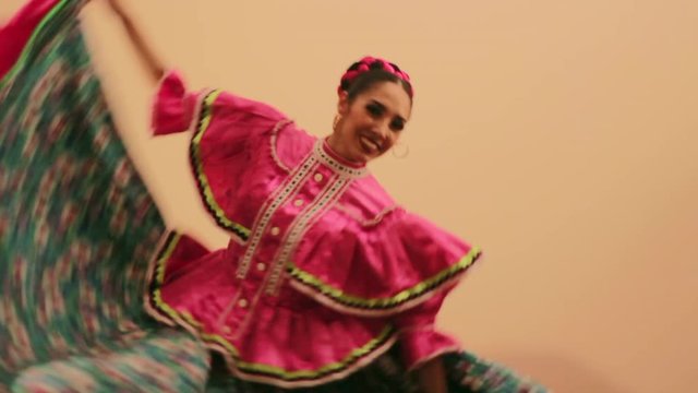 Joven mujer mexicana latina en traje regional folcl&oacute;rico en fondo rosa haciendo orlas con vestido baile danza t&iacute;pico