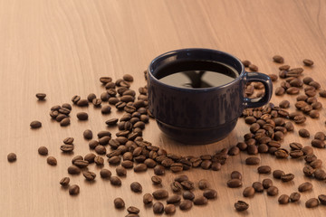 blue mug with black coffee, with coffee bean around it, on a flat wooden surface