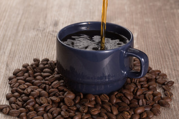 coffee serving over a blue mug, with coffee beans around it, on a flat wooden surface, closeup