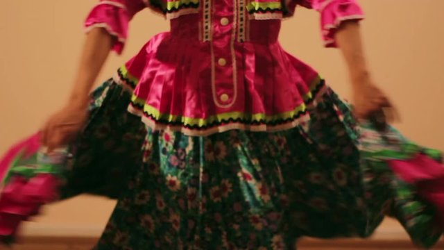 Joven mujer mexicana latina en traje regional folcl&oacute;rico en fondo rosa haciendo orlas con vestido baile danza t&iacute;pico