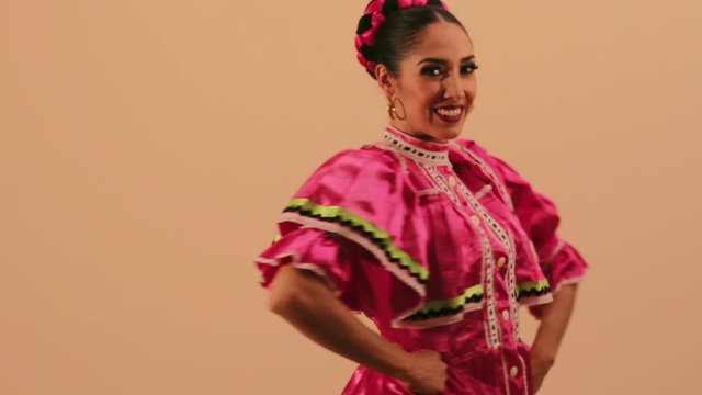 Joven mujer mexicana latina en traje regional folcl&oacute;rico en fondo rosa haciendo orlas con vestido baile danza t&iacute;pico
