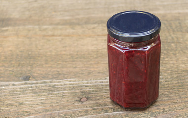 A jar of raspberries jam on a wooden background. The benefits of raspberries jam