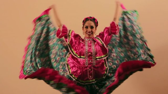 Joven mujer mexicana latina en traje regional folcl&oacute;rico en fondo rosa haciendo orlas con vestido baile danza t&iacute;pico