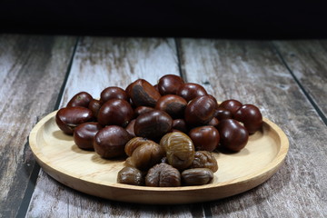 Traditional baked or roasted chestnut and peeled chestnut on the wooden plate. Famous local ingredients in Chinese cuisine. 