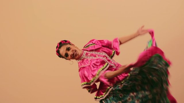 Joven mujer mexicana latina en traje regional folclórico en fondo rosa haciendo orlas con vestido baile danza típico