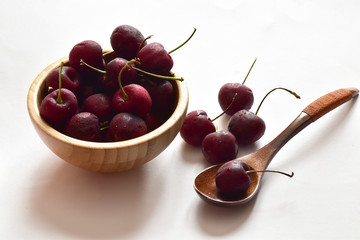 Closeup of Fresh Ripe Cherries in a wooden bowl and wooden spoon with water drops isolated on white background.