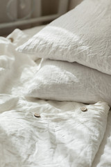 White linen textile bedclothes. Pile of pillows. Cozy bedroom interior and beautiful morning light. Pastel color. Trendy organic natural linen.