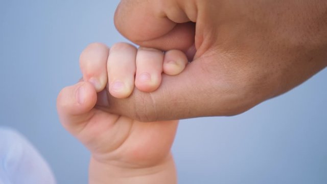 A kid hand holds the father's finger. Raising children in the family, taking care of children. Close-up of a kid's hand. Concept of family planning. A newborn child holds his father's hand.