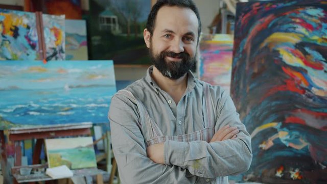 Portrait of successful artist in workshop next to abstract picture smiling and looking at camera standing with arms crossed. People and occupation concept.