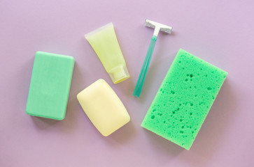 Flat lay of bath and hygiene products. Razor, soap bar and washcloth on a lilac background