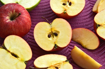Many sliced red Gala apples on purple background.
