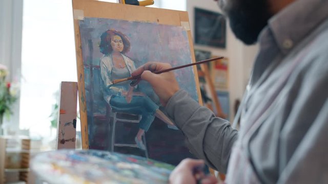 Talented male artist is creating portrait of young woman working indoors in workshop concentrated on colorful picture. Creative people and occupation concept