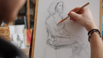 Close-up of man's hand sketching portrait of woman during lesson in art school using pencil on easel working indoors in studio - Powered by Adobe