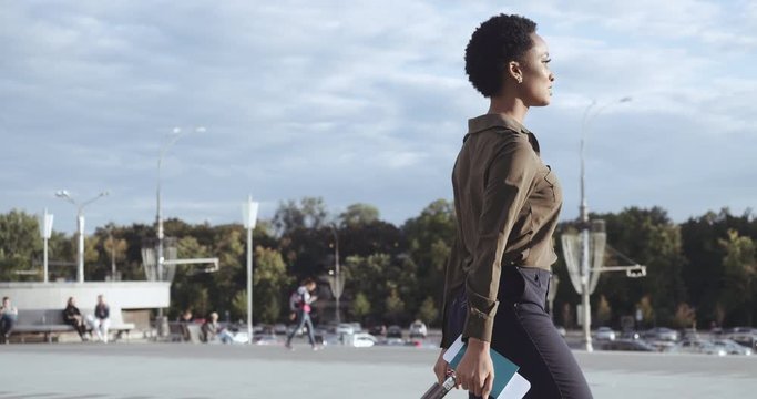 African American business woman going to taxi parking from airport terminal with luggage. Mixed race classic girl in heels stepping on street, roll baggage suitcase, travel concept, top-down shooting