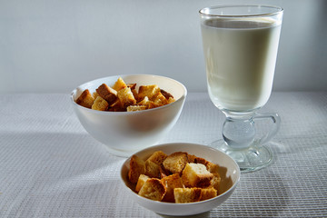 Square toasted pieces of homemade delicious rusk, hardtack, Dryasdust, zwieback and glass of milk on a white tablecloth.