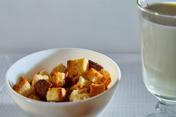 Square toasted pieces of homemade delicious rusk, hardtack, Dryasdust, zwieback and glass of milk on a white tablecloth.