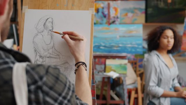 Amateur art student drawing portrait of beautiful Afro-American girl model in studio working with pencil on paper using easel busy with creative activity