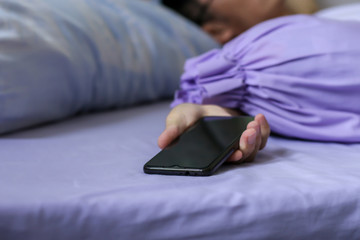 A black smartphone in man hand on purple bed