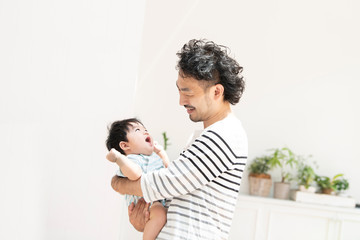 とてもいい笑顔で赤ちゃんと見つめあってて抱っこするヒゲの中年男性の横向き