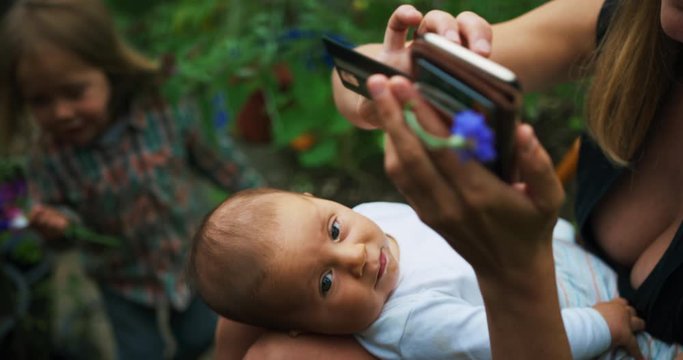 Mother with preschooler and baby using smartphone in garden