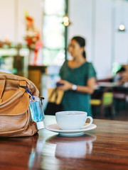 Mini alcohol gel bottle to kill Corona Virus(Covid-19) hang on a brown leather shoulder bag with hot coffee on table in cafe.New normal lifestyle.Health care concept.Selective focus on alcohol gel