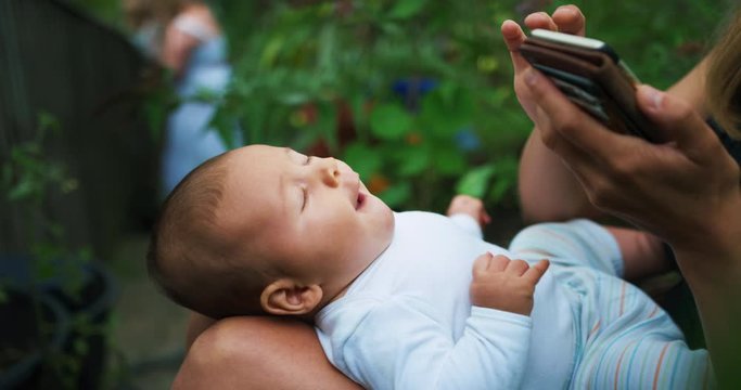 Mother with baby using smartphone in vegetable garden