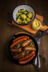 Oldenburger Grünkohl mit Pinkel, Kohlwurst, Senf und Kartoffeln in Gusseisen Pfanne auf Holz Tisch