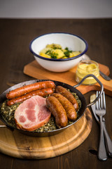 Oldenburger Grünkohl mit Pinkel, Kohlwurst, Kassler Schweine Nacken, Senf und Kartoffeln in Gusseisen Pfanne auf Holz Tisch