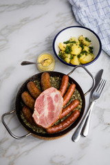 Oldenburger Grünkohl mit Pinkel, Kohlwurst, Kassler Schweine Nacken, Senf und Kartoffeln in Gusseisen Pfanne auf Marmor Tisch