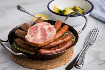 Oldenburger Grünkohl mit Pinkel, Kohlwurst, Kassler Schweine Nacken, Senf und Kartoffeln in Gusseisen Pfanne auf Marmor Tisch