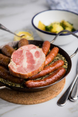Oldenburger Grünkohl mit Pinkel, Kohlwurst, Kassler Schweine Nacken, Senf und Kartoffeln in Gusseisen Pfanne auf Marmor Tisch