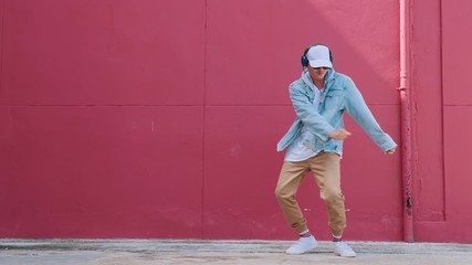 Dancing man with headphones listening to music performing various freestyle dance outdoors in street wall having fun. Modern lifestyle, happiness concept. breakdancing, hiphop dancing, street dancing. - Powered by Adobe
