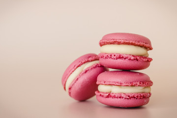 Three pink macaroon cookies with white chocolate cream on beige background