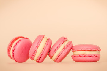 Four pink macaroon cookies with white chocolate cream on beige background