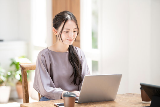 パソコンを使いながらZoomなどでリモートワークのミーティングの準備をする笑顔が美しい若い日本人女性コピースペースあり