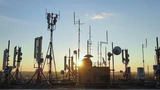 Vertigo effect footage of electromagnetic towers with satellite dish, microwaves and panel antennae on the roof during golden hour. Silhouette, Dolly zoom effect.