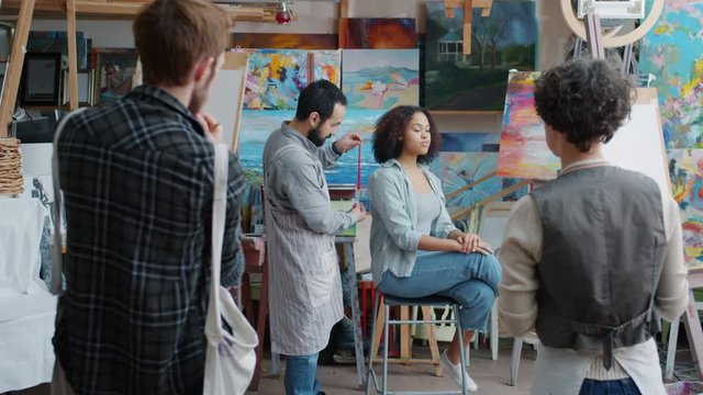 Experienced Arts Teacher Adult Man Is Speaking In Painting Class Explaining Theory To Group Of Students While Young People Are Watching And Learning