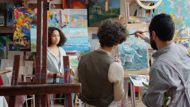 Professional artist is teaching female student painting portrait of Afro-American model with watercolors while girl is watching and learning