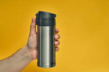 Metal mug thermos in hand on a colored background. Hot drinks on the go. Thermo mug.