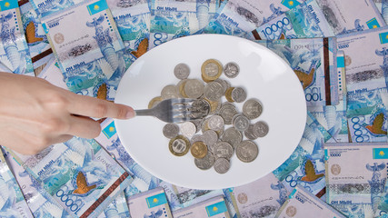 Kazakhstan tenge. Coins on a white plate. Keep money on the fork. Minimum subsistence level, food...