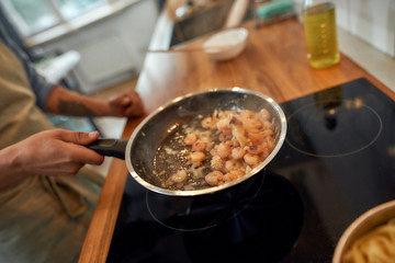 Close up of hand of man tossing shrimp with garlic and onion in the frying pan. Cook preparing dish with seafood. Mediterranean cuisine concept