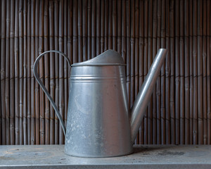 a silver watering can against bamboo fence